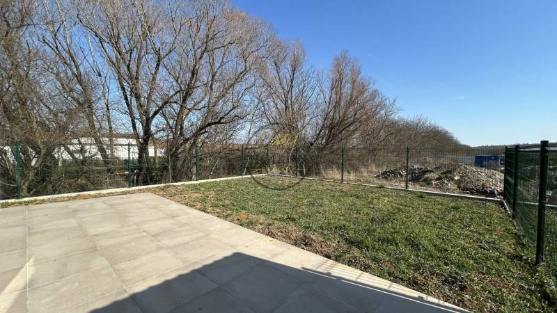 The garden of a family house in Klasov with paving and a fence in the background.