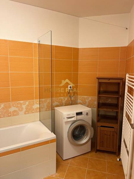 A bathroom in a 3-room apartment with orange tiles, a washing machine, and a bathtub.