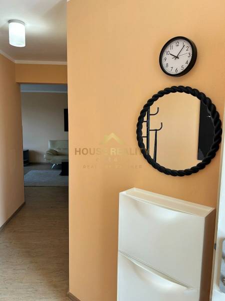 A hallway with a clock, a mirror, and a coat rack in a 3-room apartment with a wooden decor floor.