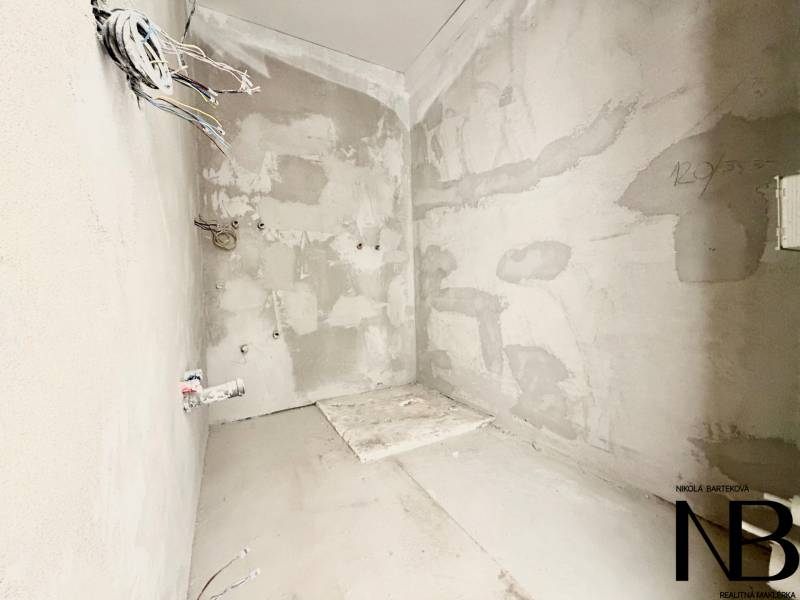 An unfinished wall with plaster and loose cables in a studio apartment.