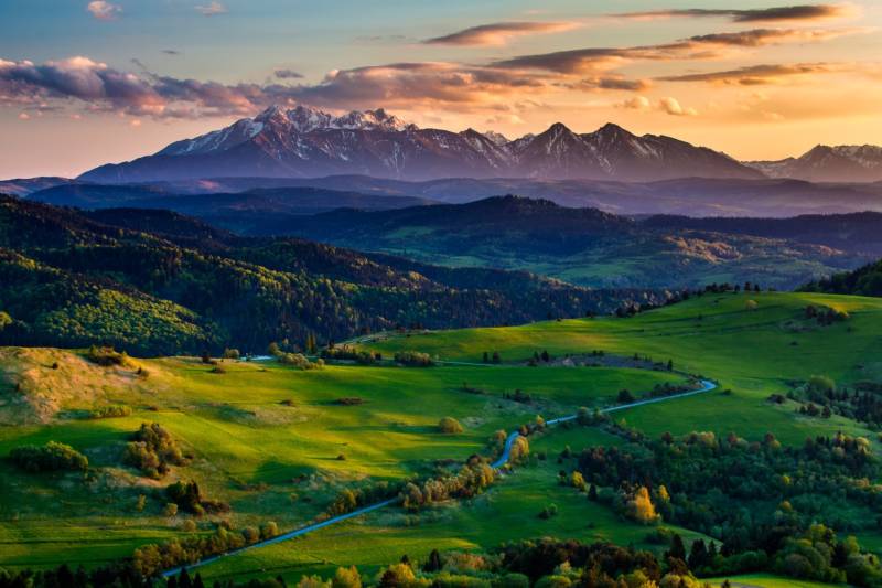 A landscape with agricultural and forest land surrounded by mountains in the Hrabkova area at sunset.