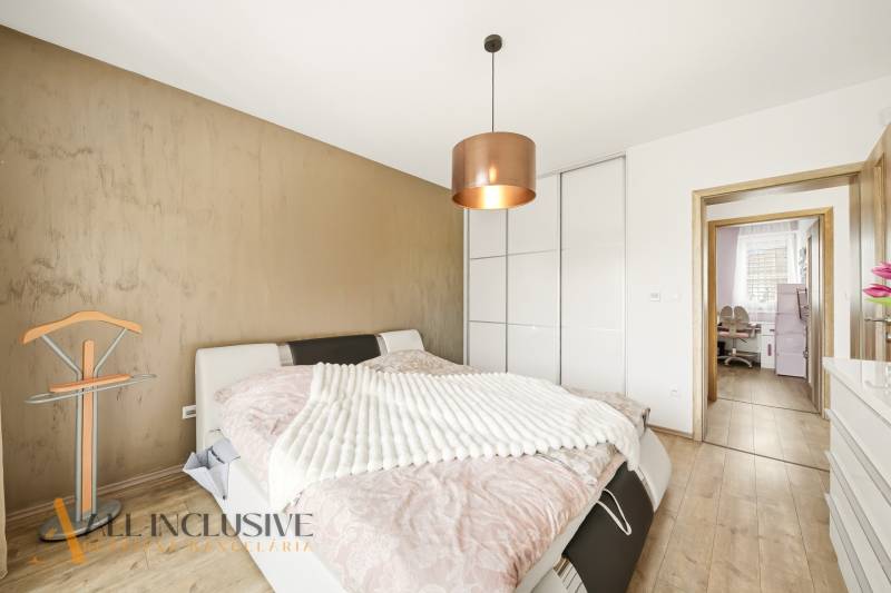 Bedroom in a family house with a bed, wardrobe, and wooden decor flooring.