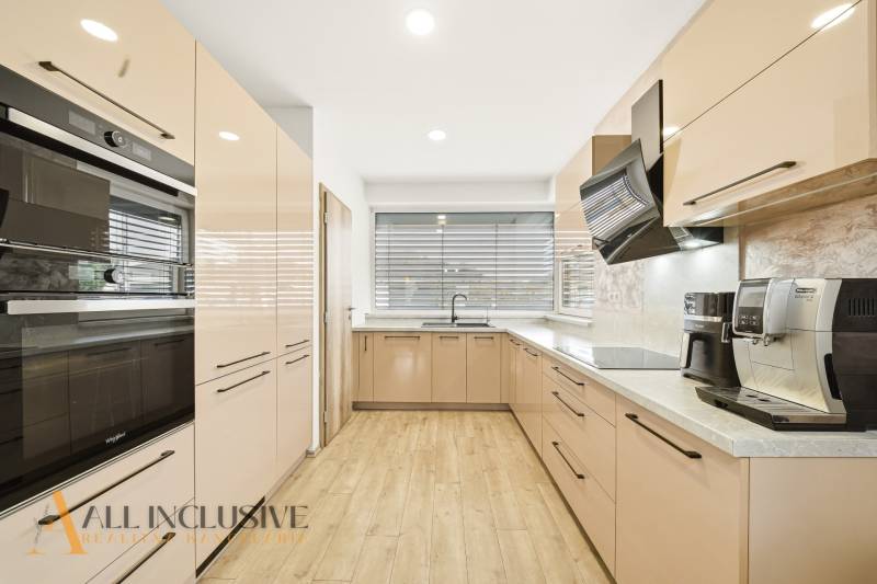 A kitchen in a family house with a wooden decor floor, equipped with appliances and large windows.