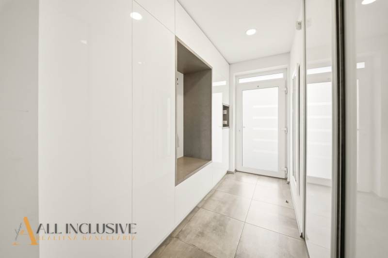 A hallway in a family house with white storage cabinets, tiles, and glass doors.