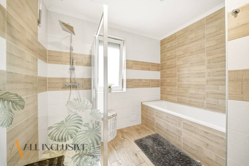 A bathroom in a family house with a bathtub, shower, and tiles with a wooden decor.