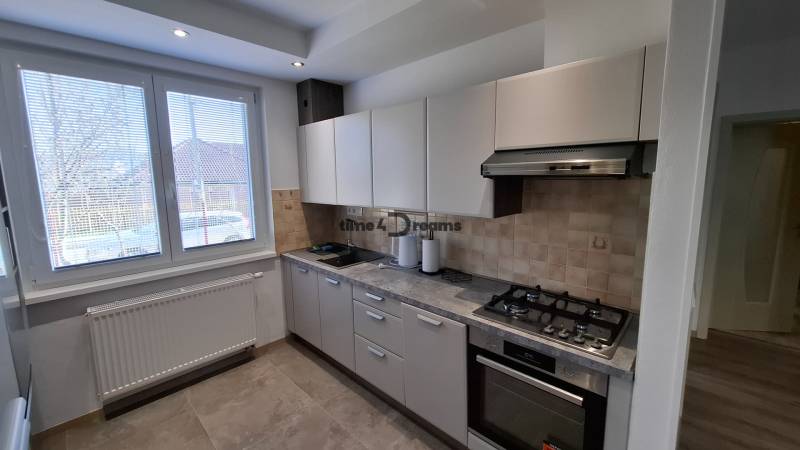 Kitchen area of a 2-room apartment with a gas stove, white cabinets, and a large window.
