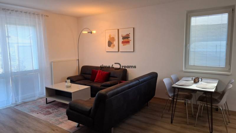 Living room in a two-room apartment with a wooden decor floor, a sofa, and a dining table.