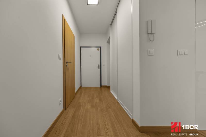 A corridor with white walls and a wooden decor floor in a 2-room apartment.
