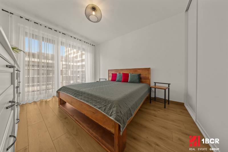 A bedroom with a bed, tables, and a wooden decor floor in a two-room apartment.