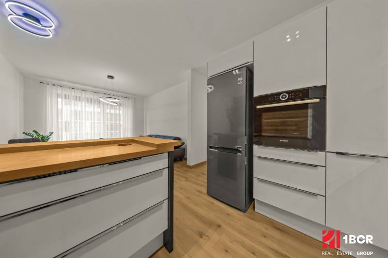 Modern kitchen in a 2-room apartment with wood-patterned flooring and stainless steel appliances.