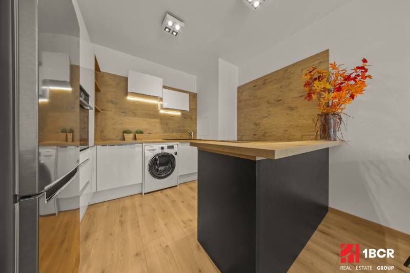 A kitchen with wooden decor, a washing machine, appliances, a floor with wooden decor, in a 2-room apartment.