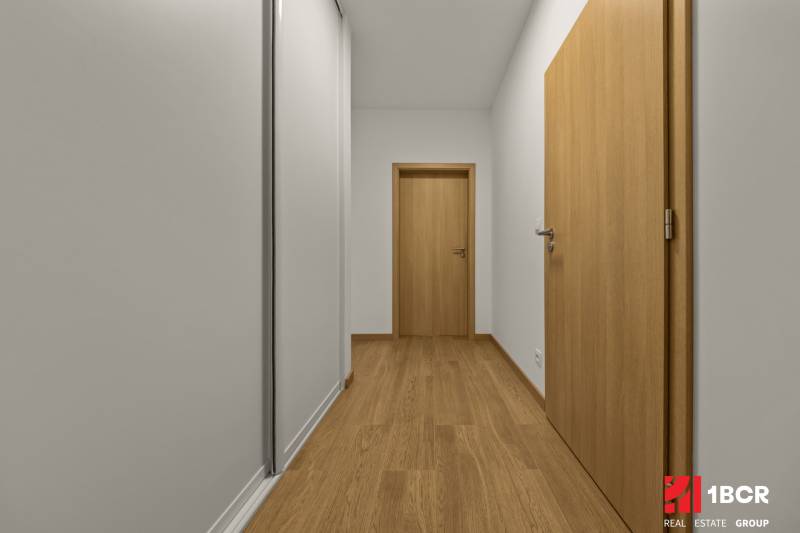 A hallway in a 2-room apartment with a wooden decor floor and wooden doors.