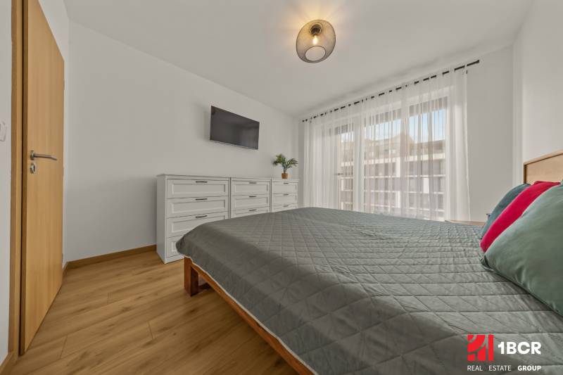 Bedroom with a TV, dresser, and bed in a 2-room apartment, floor with wood decor.