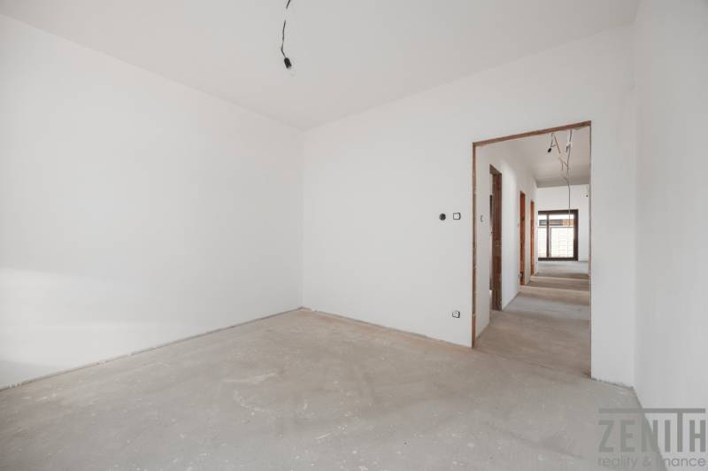 Empty room in a family house with white walls and a raw floor.