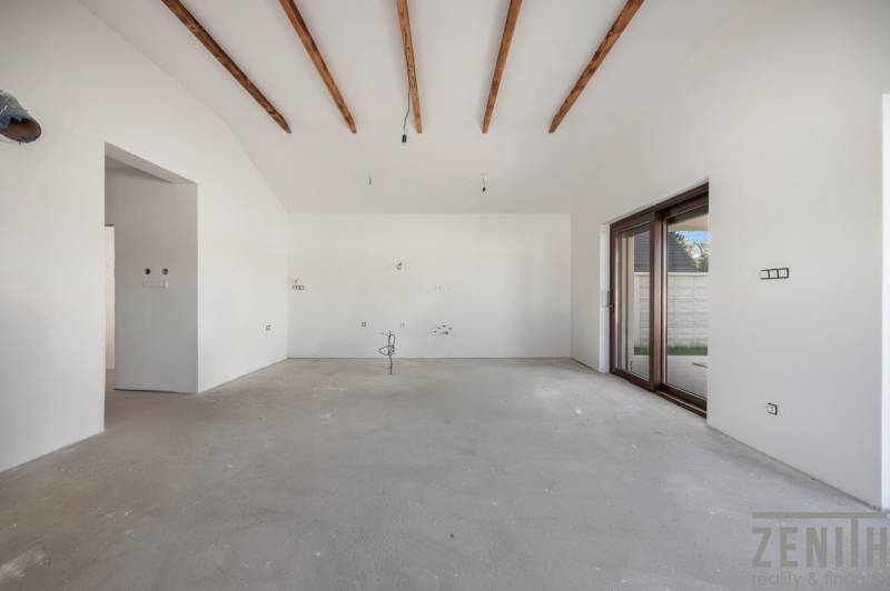 A spacious room in a family house with white walls and wooden beams on the ceiling.