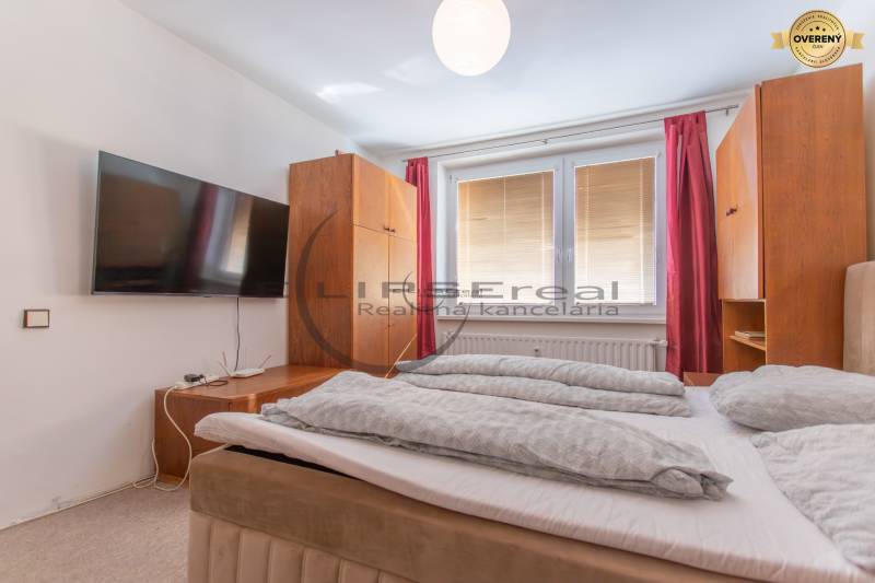 A one-bedroom apartment with a large bed, a wall-mounted TV, and red curtains.