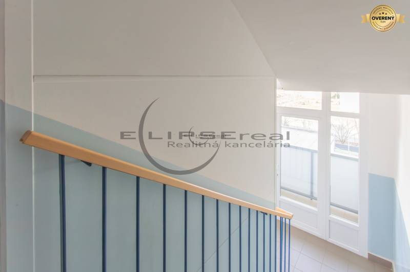A staircase with a wooden railing and a large window illuminating the space on Štúrova Street in Malacky.