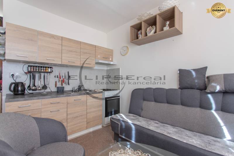 A kitchen in a one-room apartment with a kitchenette and a sofa, floor with wooden decor.