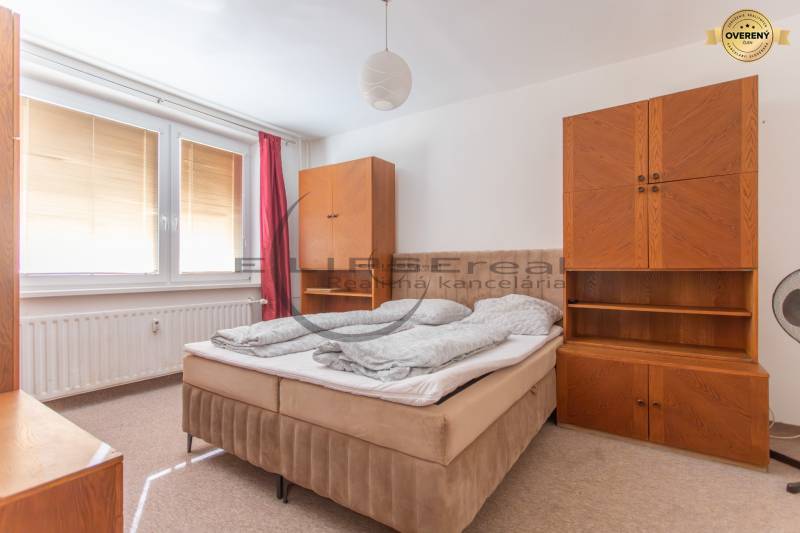 A bedroom with a bed and wooden furniture in a studio apartment, curtains on the windows.