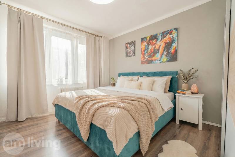 Bedroom in a 2-room apartment with a bed, paintings, and a wooden decor floor.