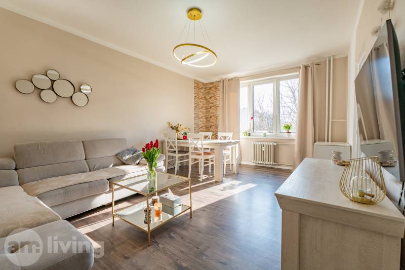 Living room with a corner sofa, dining table, and wooden decor flooring in a two-room apartment.