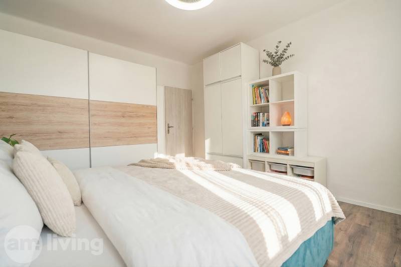 A bright bedroom with a bed, wardrobe, and shelf in a 2-room apartment with a wooden decor floor.