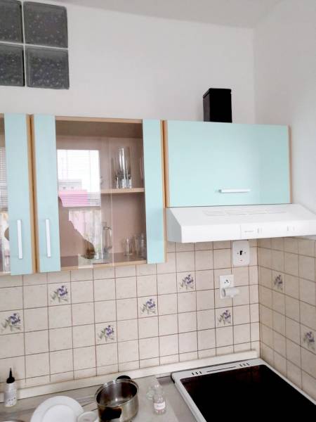 A kitchen with pastel cabinets, tiles, and a range hood in a studio apartment.