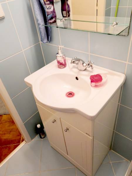A bathroom with a sink, a glass shelf, and light blue tiles in a studio apartment.