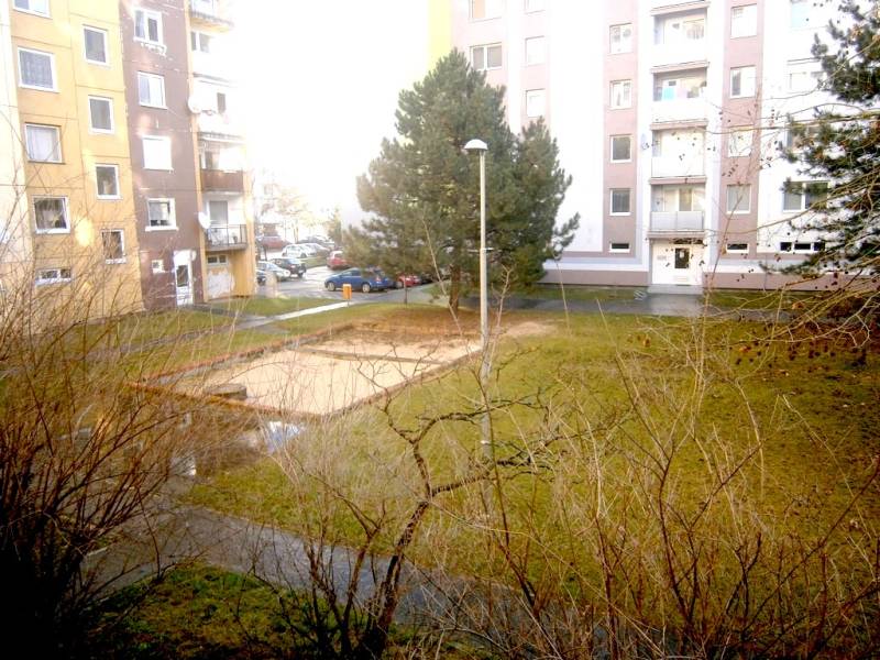 A courtyard surrounded by apartment buildings and trees in Piešťany, an ideal space for a 1-bedroom apartment.