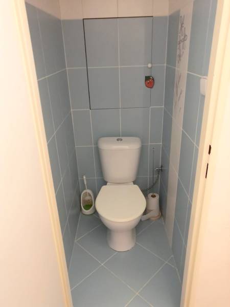 A bathroom in a one-room apartment with light blue tiles and a white toilet.