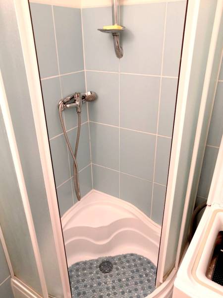 A shower corner with blue tiles and a corner in a studio apartment.