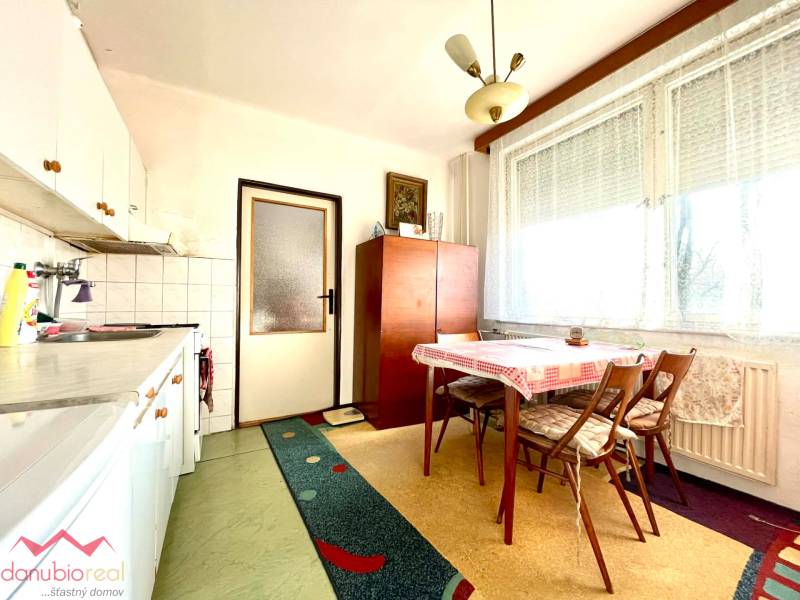 A kitchen in a studio apartment with a dining table, a patterned carpet, and a large window.