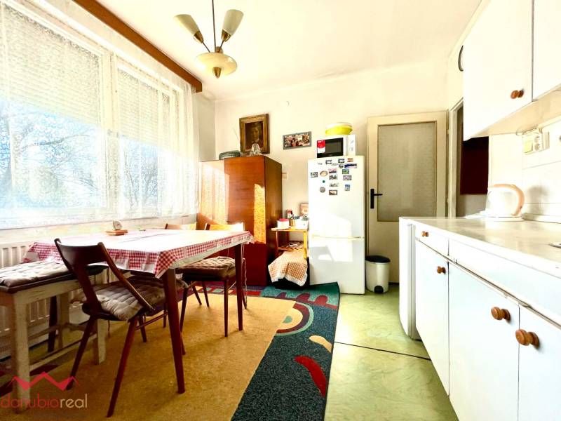 Kitchen in a studio apartment with a large window, a kitchen table, and a refrigerator.