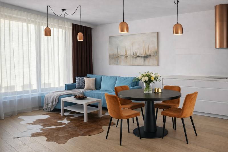 Interior of a 2-room apartment with a blue sofa, dining table, and wooden decor flooring.
