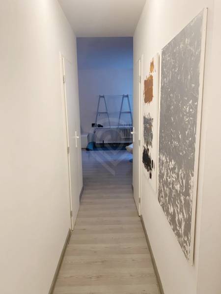 A narrow hallway in a 2-room apartment with a wooden decor floor and paintings on the wall.