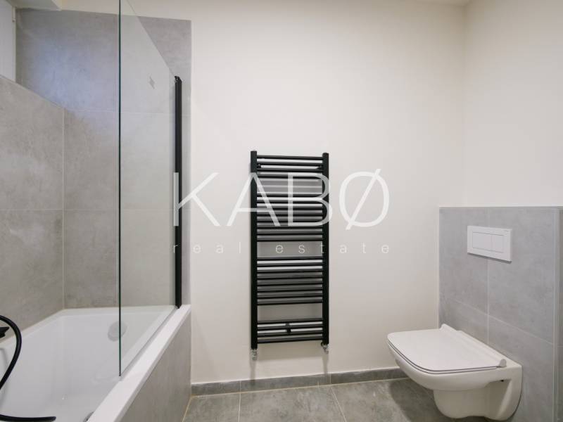 A bathroom in a family house with a bathtub, shower screen, and dark radiator.