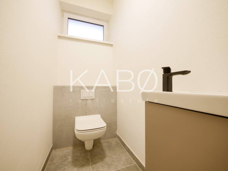 Bathroom with a sink and toilet in a family house, stone-patterned floor.