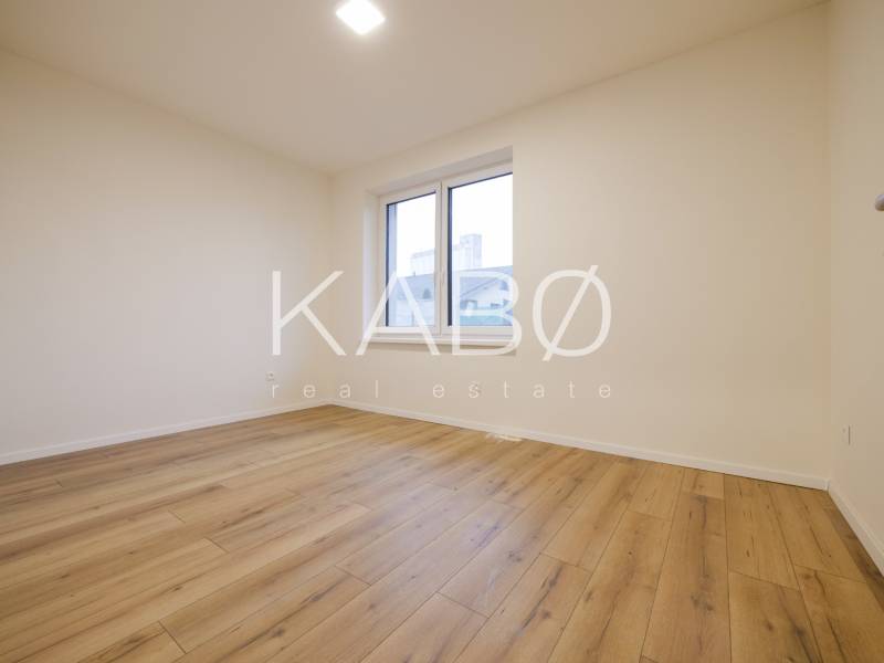 An empty room in a family house with a wood-patterned floor and a large window.