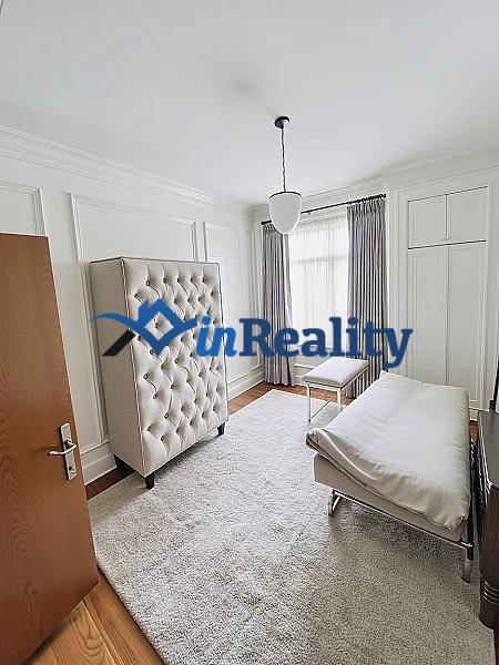 Bright bedroom in a family house with a bed, chair, and carpet on a wooden-decor floor.