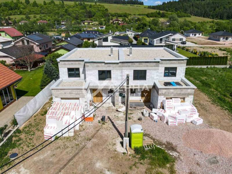 A family house under construction in Harichovce, surrounded by greenery and other houses.