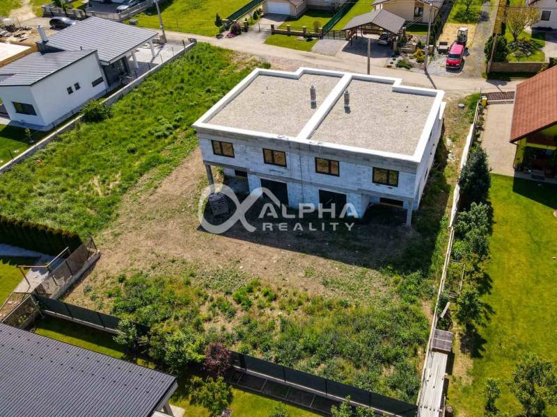A two-story family house in Harichovce with an undeveloped plot and surrounding greenery.