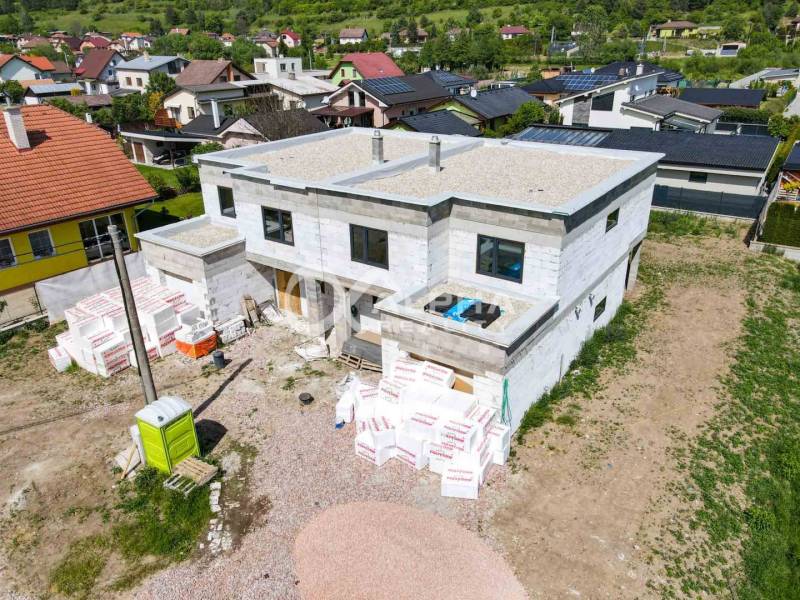 Construction of a family house in Harichovce with building materials and neighboring houses in the background.