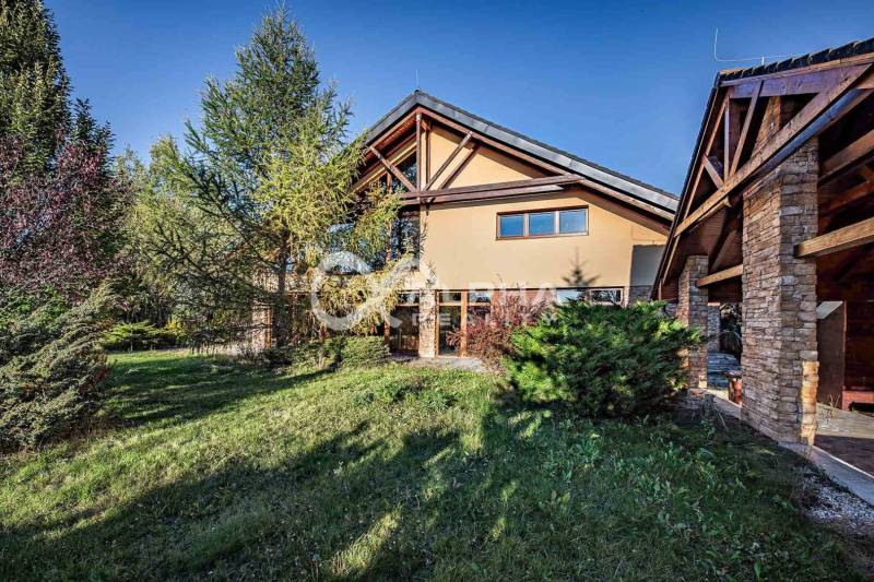 A family house in Veľká Lomnica with a grassy garden, surrounded by trees and a stone facade.