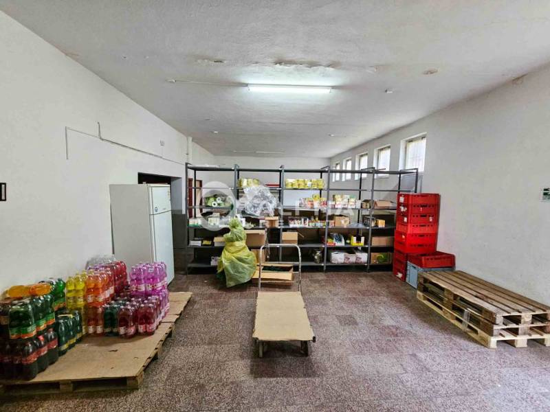 A warehouse in a building with food on shelves and drinks on pallets.