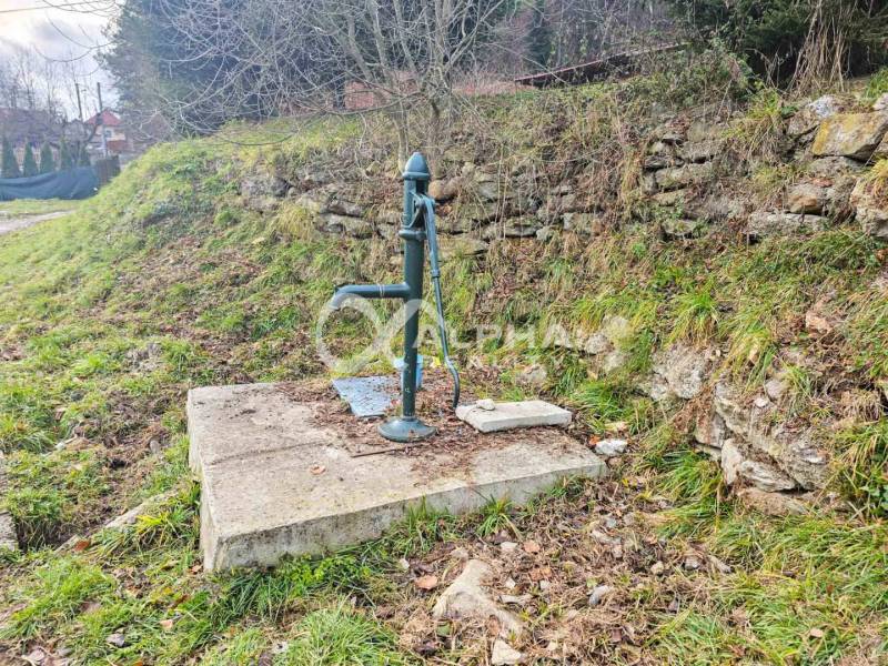 A manual pump on a concrete base next to a stone wall in Helcmanovce.