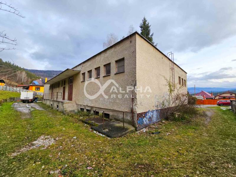 A building in Helcmanovce with grassy surroundings and neighboring houses, surrounded by hills.