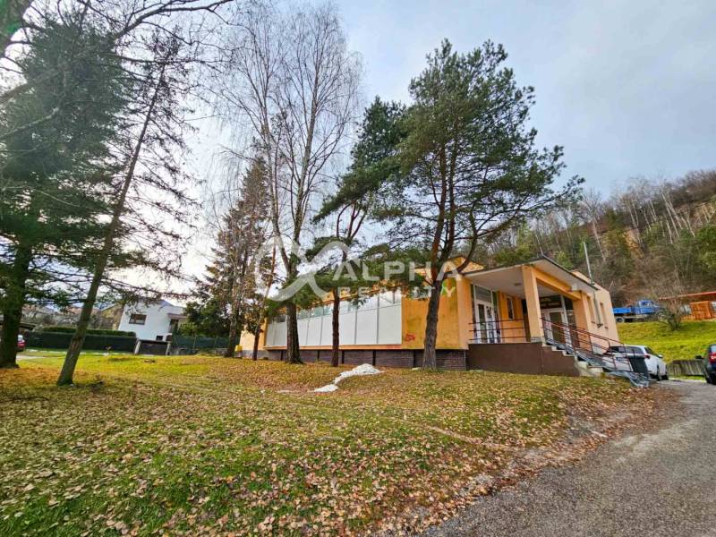 A building in Helcmanovce surrounded by trees, with a staircase leading to the entrance.