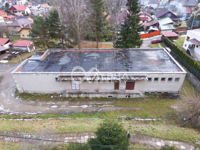 A building in Helcmanovce with a sloped roof, surrounded by greenery and other structures.