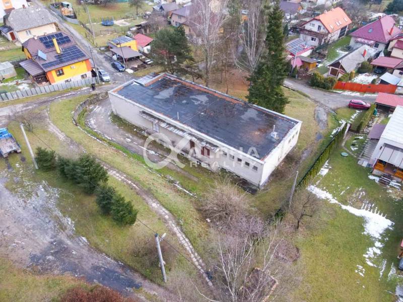 A building in Helcmanovce surrounded by greenery and other houses in a snowy landscape.