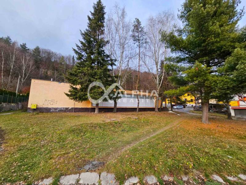 A building in Helcmanovce surrounded by trees, with a neighboring road and vehicles.